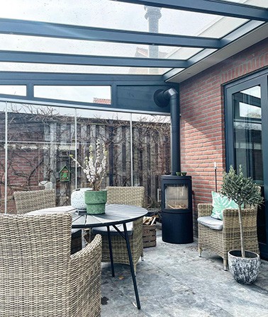 Aluminium glazen overkapping inrichten landelijk houthaard kachel veranda aan huis wicker tuinset